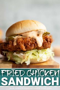 a fried chicken sandwich with lettuce and sauce on it, sitting on a cutting board