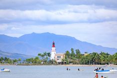 several boats are in the water near a light house and palm trees with mountains in the background