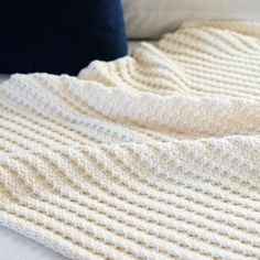 a white crocheted blanket laying on top of a bed next to a pillow