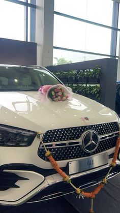 a white mercedes benz car with flowers on the hood and front grill, parked in a showroom