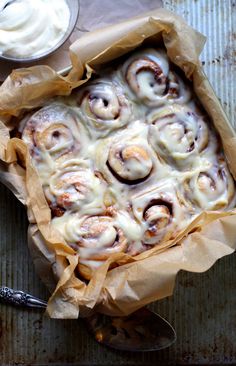 a pan filled with cinnamon rolls next to a bowl of cream cheese and a spoon