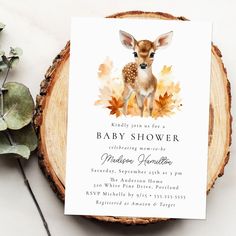 a baby shower card with a deer and leaves on it next to a wooden slice