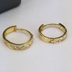 Beautiful hoop earrings in 14k gold with synthetic zirconia stones. All for only $85 Hoop measures 2mm width, 9mm circumference, and a clip-on closure. Purchase includes a gift box. Gold Plated Hallmarked Huggie Earrings, Gold Cubic Zirconia Huggie Earrings Round Cut, Gold Channel Set Huggie Jewelry, Gold Cubic Zirconia Huggie Ring, Classic Gold Huggie Earrings Channel Set, Gold Round Cut Huggie Earrings, Classic Gold Channel Set Huggie Earrings, Yellow Gold Cubic Zirconia Channel Set Huggie Earrings, Gold Channel Set Hoop Earrings