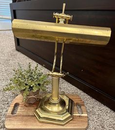 a brass desk lamp sitting on top of a wooden stand next to a potted plant