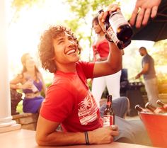 a young man sitting on the ground drinking from a bottle while people stand in the background