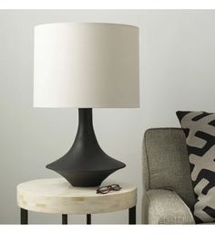 a black lamp sitting on top of a table next to a chair and ottoman cushion