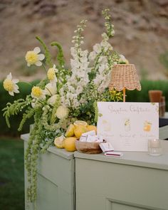 an arrangement of flowers, lemons and other items on a table with a sign