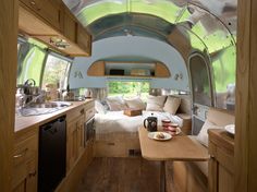 the interior of a camper with wood flooring and walls, windows, and cabinets