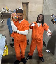 two men dressed in orange prison uniforms holding up candy bags while standing next to each other