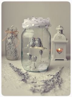 two glass jars filled with tiny birds sitting on top of a table next to candles