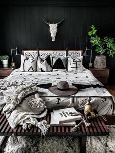 a bed with black and white decor in a dark colored room, surrounded by plants