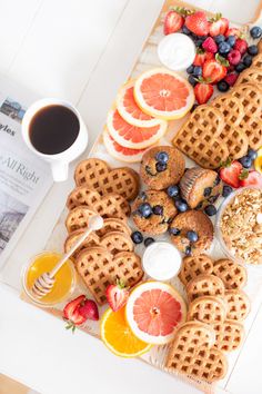 a table topped with waffles and fruit next to a cup of coffee