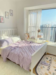 a white bed sitting next to a window in a bedroom under a purple comforter