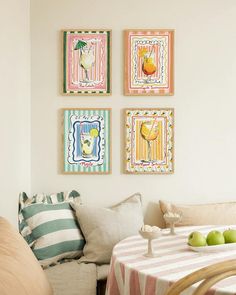 four framed pictures hang on the wall above a dining room table with apples and two chairs