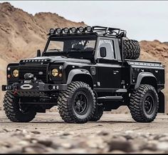 a large black truck parked on top of a dirt field next to rocks and mountains