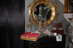 a mirror and some candles on a dresser in front of a black curtain with gold trim