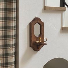 a mirror mounted to the side of a white wall next to a plaid shower curtain