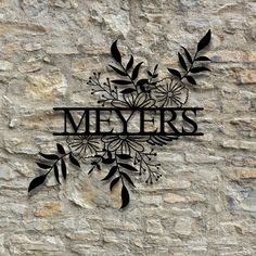 a metal sign that says meyers with flowers and leaves on the side of a stone wall