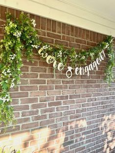 a brick wall with greenery hanging from it's sides and the word love is engagement spelled in cursive letters