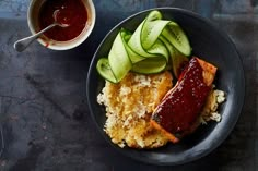 a black plate topped with rice and meat covered in cucumbers next to a cup of ketchup