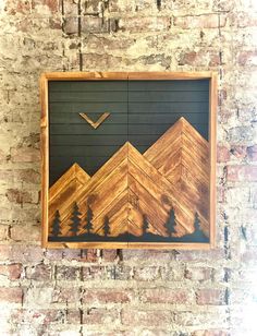 a wooden frame with mountains and trees on it hanging on a brick wall in front of a brick wall