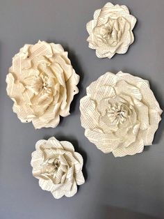 three large white flowers are hanging on the wall in front of a gray background, and one is made out of fabric