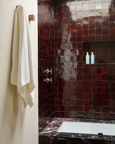 a white towel hanging on the wall next to a bathtub in a bathroom with red tiles