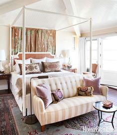 a white bed sitting next to a couch on top of a carpeted bedroom floor