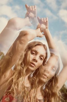 two beautiful young women standing next to each other in front of a blue sky with clouds