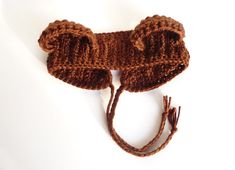 a brown knitted bear hat on a white surface with string attached to it's ear