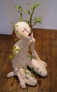 a white statue sitting on top of a wooden floor next to a plant growing out of it's head