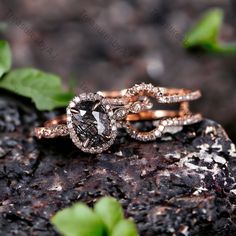 two wedding rings on top of a rock with leaves around the band and one has a black diamond surrounded by white diamonds