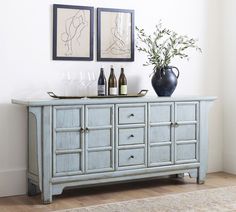 a blue buffet table with bottles and glasses on it in front of two framed pictures