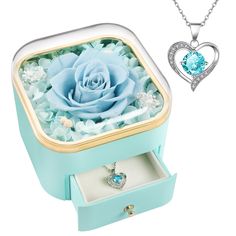 a jewelry box with a blue rose in it next to a heart shaped necklace and ring