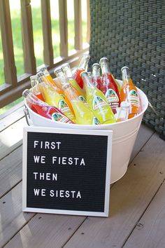 a white bucket filled with lots of different types of drinks next to a sign that says first we fiesta then we siesta