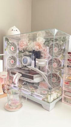 a display case with flowers and other items in it on a white countertop next to a lamp