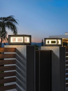 two lights that are on the side of a building near a fence and palm tree