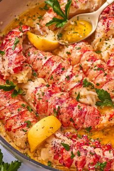 a pan filled with lobster and pasta next to lemon wedges, parsley and parsley