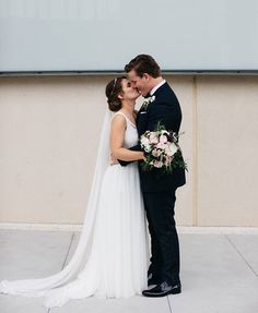 a bride and groom kissing in front of a large screen on the side of a building