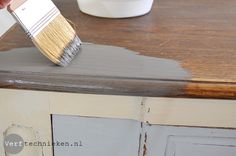 a person is using a brush to paint the side of a cabinet