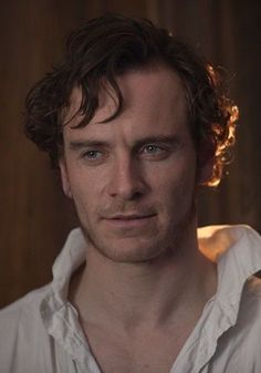 a man with curly hair and blue eyes looks at the camera while wearing a white shirt