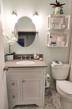 a white toilet sitting next to a sink in a bathroom under a mirror and shelves