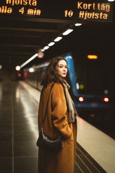 a woman standing in front of a train at a subway station, waiting for her train