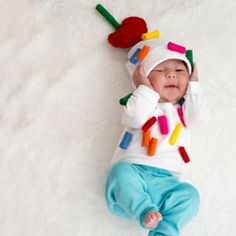 a baby laying on its back wearing a hat and sweater with crayons all over it