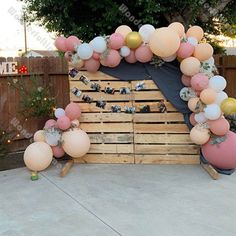 an arch made out of wooden pallets with balloons and decorations on the top, in front of a fence