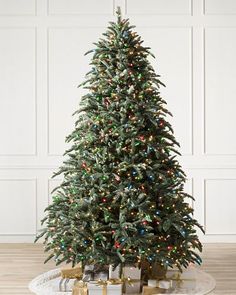 a christmas tree with presents under it on a white rug in front of a wall