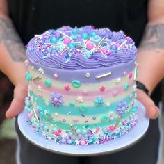 a person holding a colorful cake with sprinkles on it's side