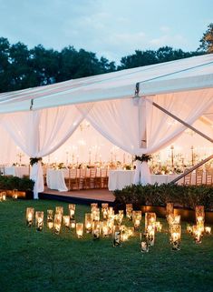 many candles are lit up in front of a tent with white drapes and curtains