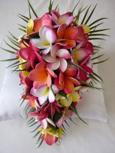 a bouquet of pink and yellow flowers sitting on top of a white pillow with palm leaves