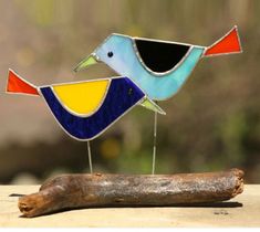 two stained glass birds sitting on top of a piece of wood